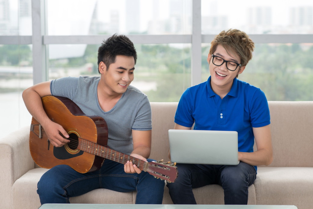Handsome guy playing the guitar while his friend surfing the internet